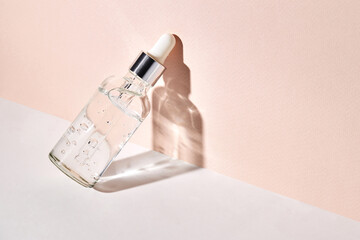 Skin care essence, emulsion or serum in glass transparent bottle with dropper on white and beige background. Hydrating serum, vitamin for face skin. 