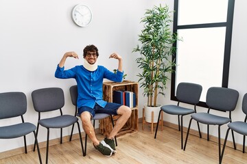 Young hispanic man sitting at doctor waiting room with neck injury looking confident with smile on face, pointing oneself with fingers proud and happy.