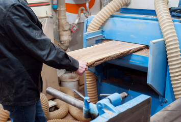 A male carpenter works in a carpentry workshop on a thickness gauge. planing wood
