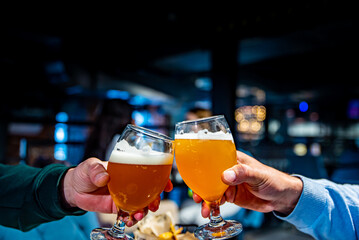 two glass of beer in hand. Beer glasses clinking in bar or pub - obrazy, fototapety, plakaty