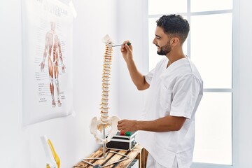 Young arab man wearing physiotherapist uniform pointing to vertebral column at clinic