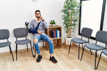 Young arab man injured smiling confident talking on the smartphone at clinic waiting room