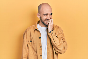 Young bald man wearing casual clothes looking stressed and nervous with hands on mouth biting nails. anxiety problem.