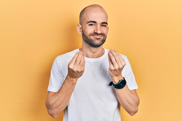 Young bald man wearing casual white t shirt doing money gesture with hands, asking for salary payment, millionaire business