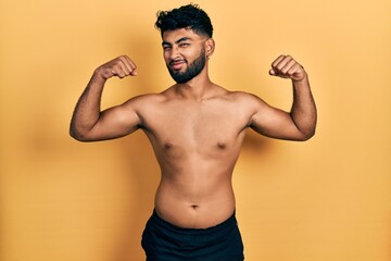 Arab man with beard wearing swimwear shirtless showing arms muscles smiling proud. fitness concept.