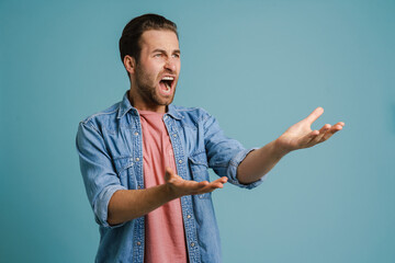 Young furious man wearing shirt gesturing and screaming at camera