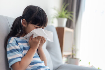 Unhealthy kid blowing nose into tissue, Child suffering from running nose or sneezing, A girl...