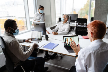 Multiracial colleagues in face masks talking during meeting at office