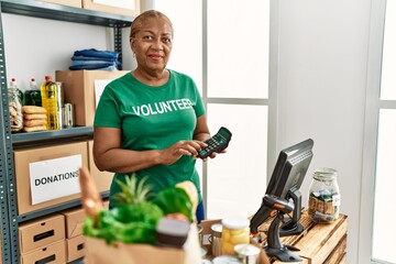Senior african american woman wearing volunteer uniform using calculator at charity center