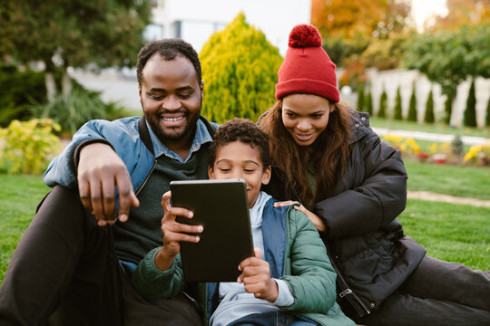 Black Family Using Tablet Computer While Resting Together On Backyard