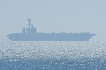 US Navy aircraft carrier sailing on the horizon.