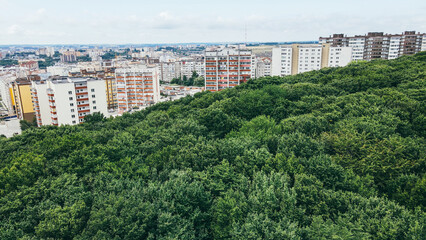 Fototapeta na wymiar Aerial flight over large overgrown green wild forest overlooking city buildings