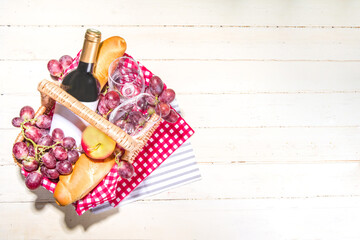 Picnic basket with food, wine bottle, glasses and fruits on green sunny lawn grass 