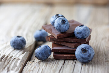 Dark chocolate stack and fresh organic blueberries on wooden table. Natural light, selective focus.