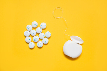 Dental floss and mint-flavored round chewing gums on a yellow background. The concept of oral care and caries prevention. Dental care products and oral hygiene. Modern dental care