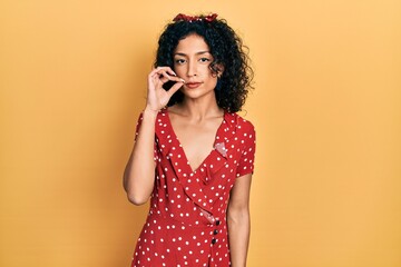 Young latin girl wearing summer dress mouth and lips shut as zip with fingers. secret and silent,...