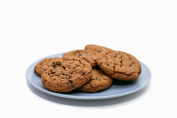 Chocolate chip cookies lie on a plate on a white background. Sweet homemade chocolate chip cookies. American style breakfast with milk or coffee in the form of chocolate chip cookies