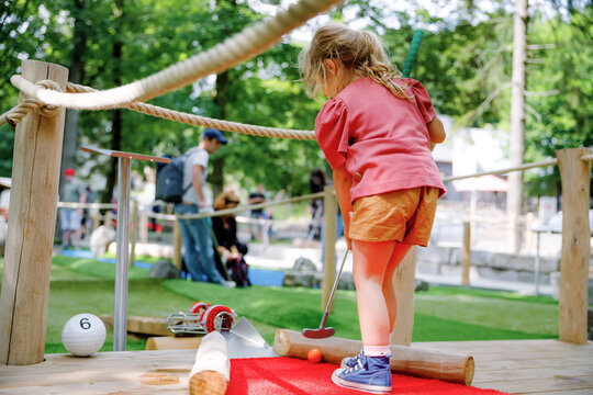 Cute preschool girl playing mini golf with family. Happy toddler child having fun with outdoor activity. Summer sport for children and adults, outdoors. Family vacations or resort.
