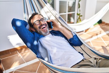 Middle age man talking on the smartphone lying on hammock at terrace home