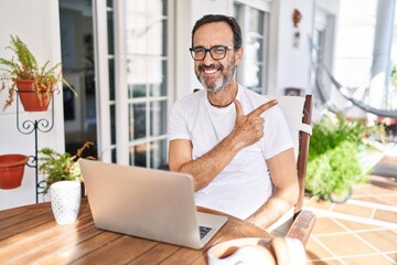 Middle age man using computer laptop at home cheerful with a smile on face pointing with hand and finger up to the side with happy and natural expression