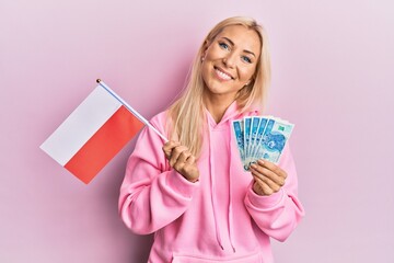 Young blonde woman holding poland flag and zloty banknotes smiling with a happy and cool smile on face. showing teeth.