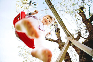 Happy little toddler girl having fun on swing in domestic garden. Smiling positive healthy child...
