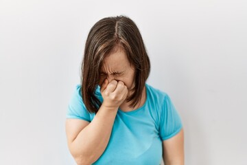 Young down syndrome woman standing over isolated background tired rubbing nose and eyes feeling fatigue and headache. stress and frustration concept.