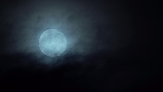 Bright white full moon rising in the sky - Dark mystical clouds passing in front while moon slowly moving upwards in frame