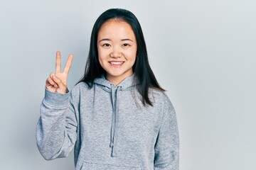 Young chinese girl wearing casual clothes smiling with happy face winking at the camera doing victory sign. number two.