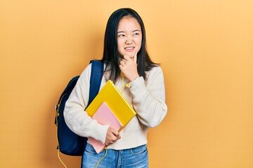 Young chinese girl holding student backpack and books thinking worried about a question, concerned and nervous with hand on chin