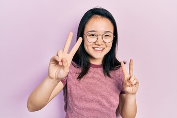 Young chinese girl wearing casual clothes and glasses smiling looking to the camera showing fingers...