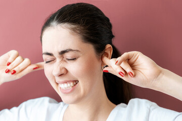 Portrait of a stressed young Caucasian woman covering her ears from pain or loud sound. Reddish...