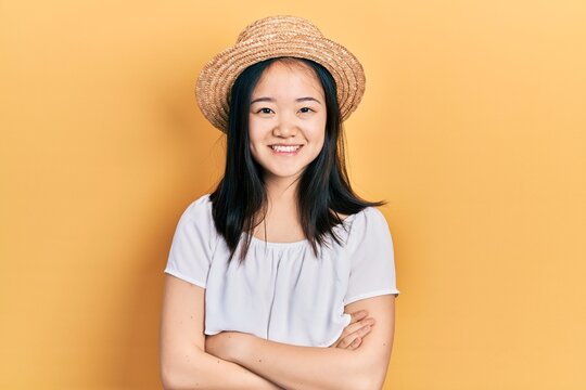 Young chinese girl wearing summer hat happy face smiling with crossed arms looking at the camera. positive person.