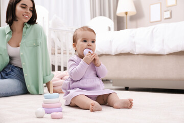 Cute baby girl playing with toy pyramid near mother on floor at home