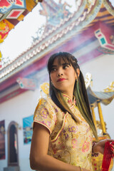 Fototapeta premium Beautiful Asian woman wearing traditional yellow cheongsam qipao dress standing and looking away in Chinese temple in Chinese new year festival.