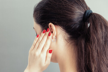 A young caucasian woman closes her ear with her fingers with a red manicure in pain or a loud...