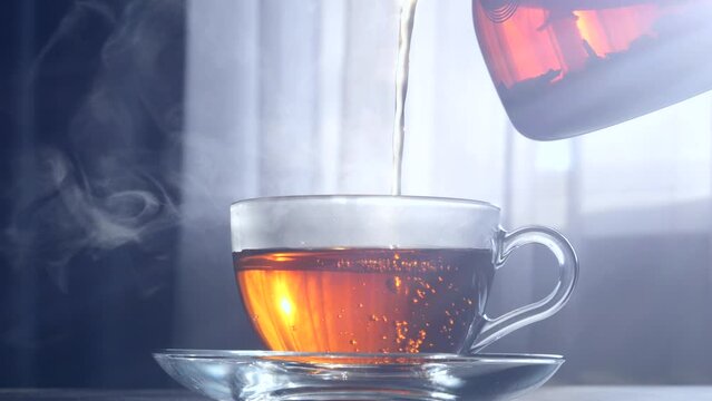 Black tea is poured from a teapot into a glass cup 