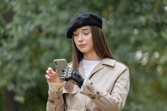 a happy European cyber woman in a raincoat with a bionic prosthesis on her arm is chatting on the phone with friends. disability or amputation of limbs, bionic prosthetics of the forearm, hand and