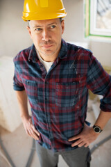 Portrait of construction worker on building site with yellow safety helmet and checkered shirt in an interior room or loft