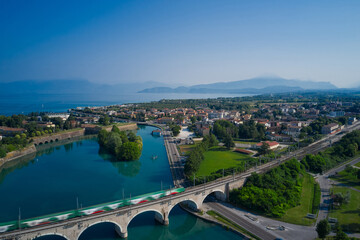 Peschiera del Garda, Italy. Train passes an arched railway bridge over a river in the background...