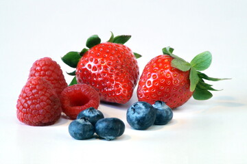 On the table are fresh juicy raspberries, strawberries, blueberries photographed close-up.