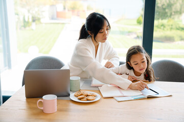 Asian girl doing homework with her mother in kitchen