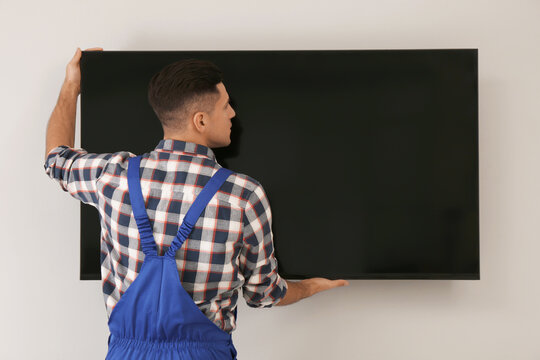 Professional technician installing modern flat screen TV on wall indoors