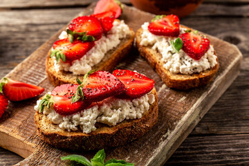 toasts or bruschetta with strawberry and mint on cream cheese ricotta. Delicious breakfast or snack, top view