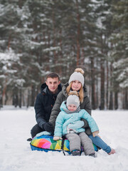 Happy family, little daughter and parents. Winter entertainment, tubing