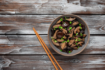 Fried shiitake mushrooms with green onions in a bowl on a wooden old background. Japanese vegetarian food. Top view, selective focus.