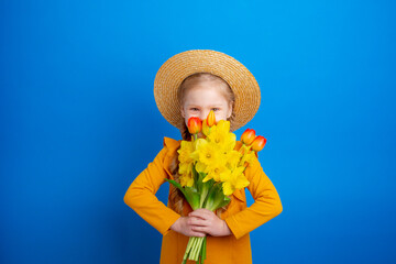 cute little girl in a straw hat hide, holding a bouquet of spring flowers on a blue background,