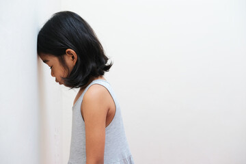 Side view of Asian kid showing sad expression with her head on the wall - obrazy, fototapety, plakaty