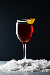 Cose-up red wine glass standing in snow with slice of orange on edge,rim decorated with sugar,dark blue background,rear-side light.Mulled wine winter holiday drink concept.Copy space, selective focus.