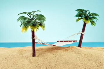 Miniature hammock on artificial palm trees. Layout of the beach with palm trees in the sand. Blue sky in the background. The concept of rest and travel.